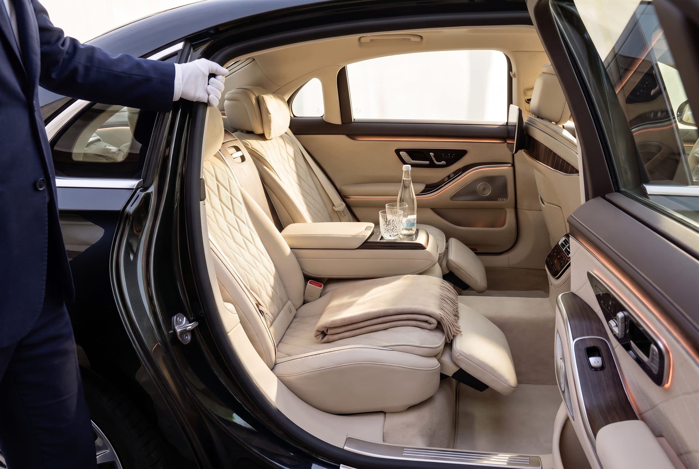 Cream quilted leather rear seat of a Mercedes S-Class with footrest, blanket and chilled water