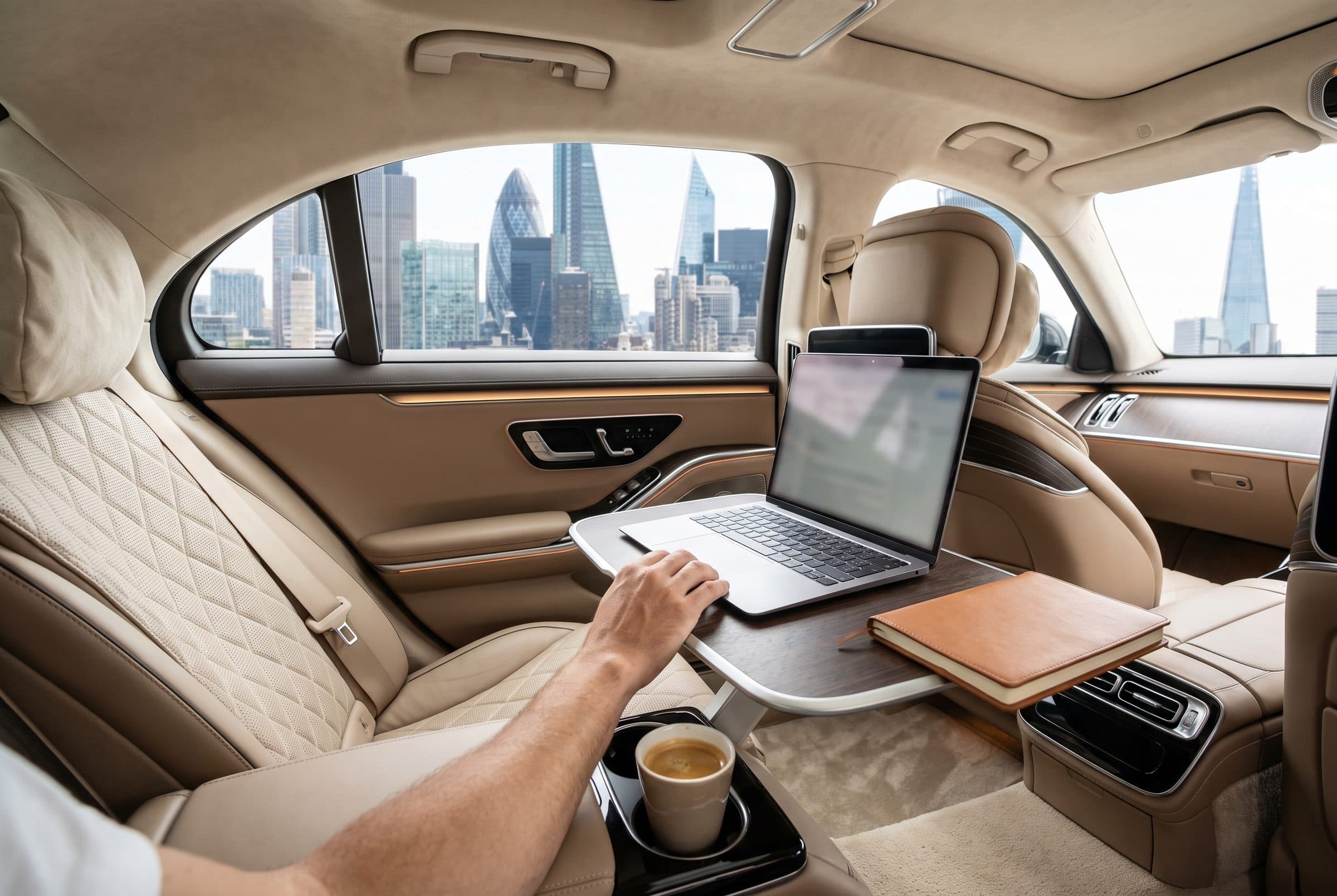 Laptop and coffee on the rear table of a Mercedes S-Class with the City of London skyline outside
