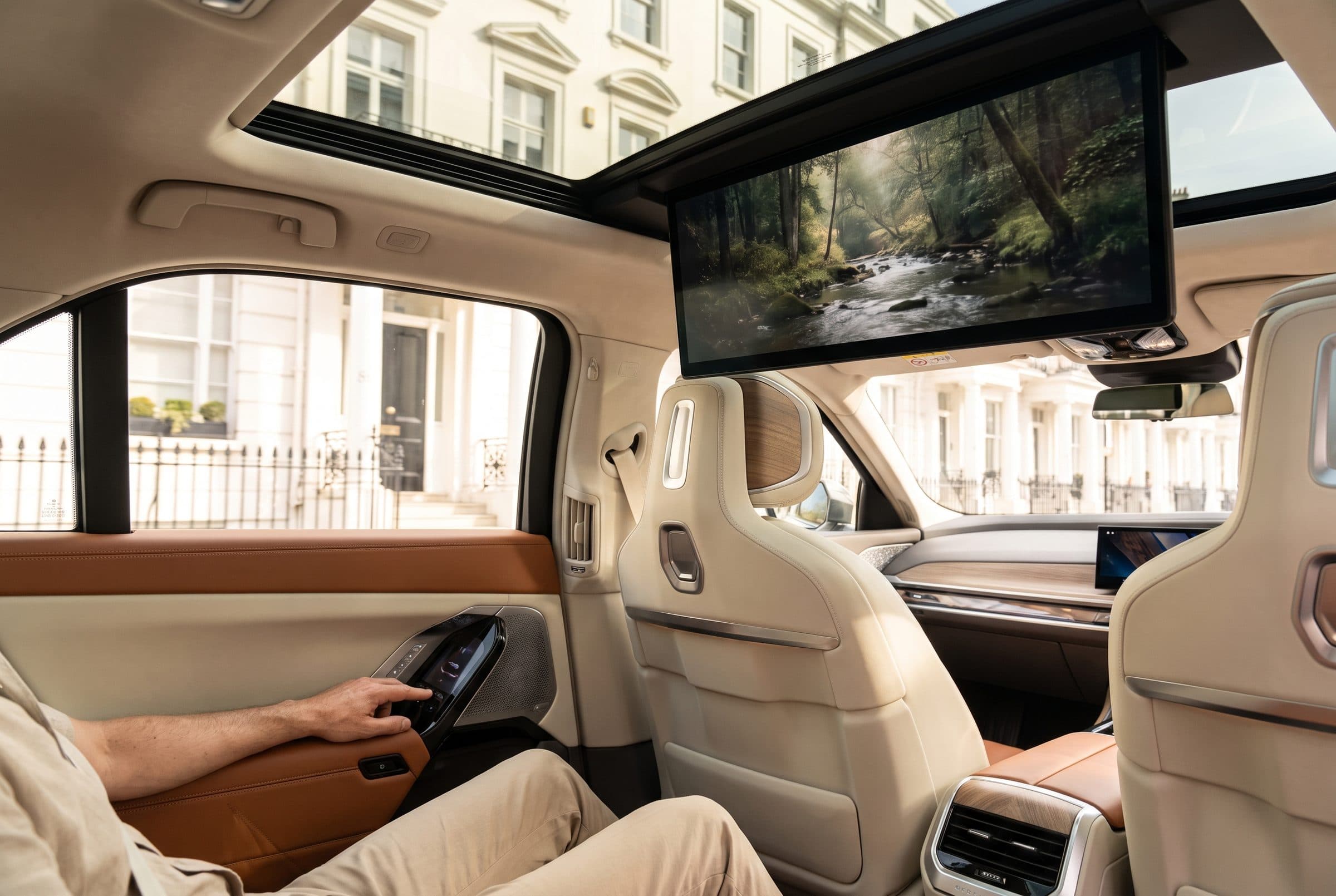 BMW i7 rear cabin by day with the theatre screen lowered and Belgravia townhouses outside