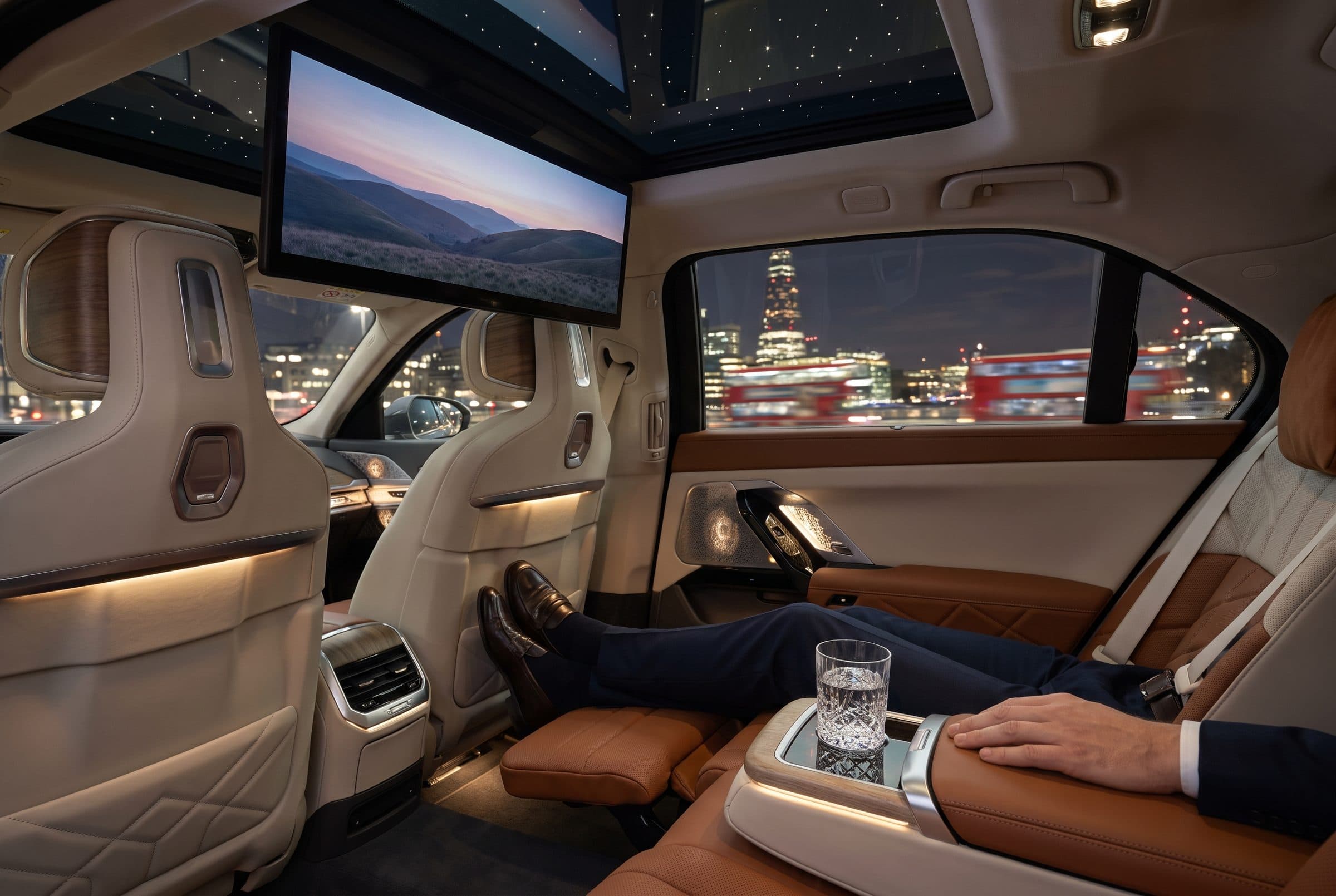 Reclined rear lounge seat of a BMW i7 at night with the 31-inch theatre screen down and a starlit roof