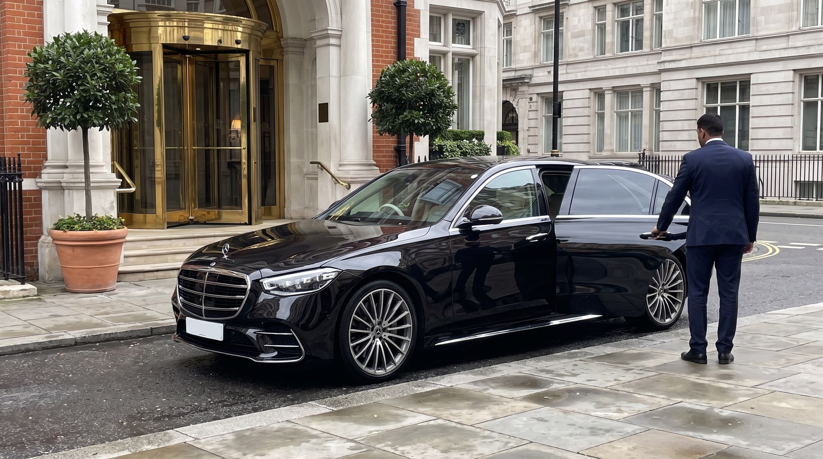 Chauffeur in a navy suit holding the rear door of a black Mercedes S-Class outside a Mayfair hotel